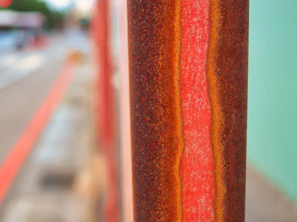 Uzun, paslı bir metal kiriş odak noktasında duruyor, arkasında yeşil inşaat çitleri ve bulanık binalar var..