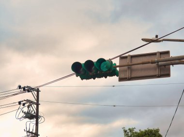 Metal bir direğin tepesine yeşil bir trafik lambası monte edilir. Elektrik hatları bulutlu bir gökyüzüne doğru ilerler..