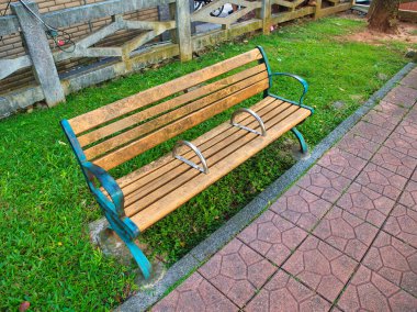 Metal kolları ve bisiklet kilitleri olan eskimiş ahşap bir bank kaldırım yollarının yanındaki çimlere oturur..