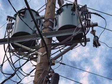 An electric pole with multiple wires and transformers stretches against a backdrop of a cloudy sky. clipart