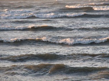 Açık denizde, berrak bir gökyüzünün altında yuvarlanan beyaz kaplama dalgalar ritmik ve dingin bir okyanus manzarası yaratıyor..