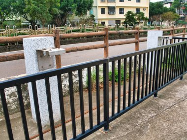 Granite water fountains with modern taps are bordered by a wooden railing and black metal fence, set against grassy surroundings near a walkway. clipart