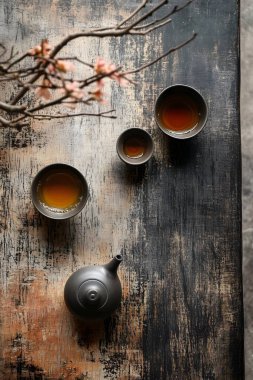 A minimalist tea ceremony setting featuring three tea cups and a teapot on a textured wooden surface.  clipart