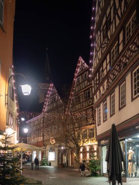 Bir sürü bina ve yürüyen insanlarla dolu bir cadde. Binalar ışıklarla süslenmiş ve arka planda bir saat kulesi var. Manzara şenlikli ve canlı