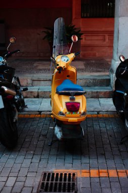 Caddedeki iki siyah siyah motosikletin arasında parlak sarı motosiklet. Motosikletin rengi sarı çizgilerle uyuşuyor.