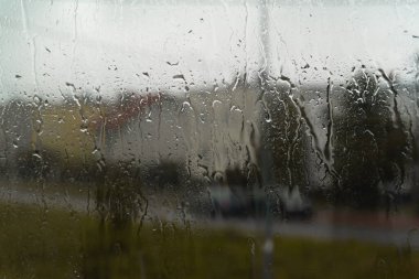 Arkaplanda bulanık bir manzara olan yağmur damlaları pencere camına saçıldı. Su damlacıkları yumuşak manzaraya karşı keskin bir şekilde duruyor, rahatlatıcı bir görüntü yaratıyor. Yağmurlu bir gün..