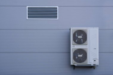 Endüstriyel bir binada klima kompresörleri ve kondansatörleri olan bir havalandırma ünitesi. Binanın soğutma ve havalandırma sistemi için gerekli olan ekipman, istikrarlı bir iklim kontrolü sağlıyor.