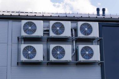 Endüstriyel havalandırma üniteleri bir binanın duvarına kurulmuş, arkasında açık mavi bir gökyüzü ve bulutlar var. HVAC sistemi.