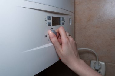 Merkezi gaz ısıtma panelinin ısı kontrolünü ayarlayan bir kadın elinin yakın çekimi..