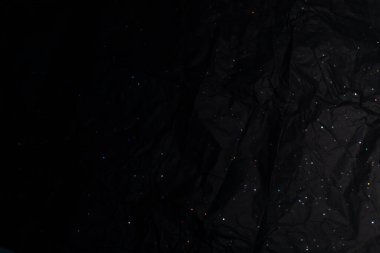 Holografik gökkuşağı benekleri etrafa saçılmış siyah buruşmuş kağıt. Dokulu yüzey ve yanardöner yansımalar büyüleyici, galaksi benzeri bir zemin yaratır..