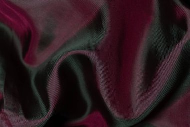 Dalgalı sentetik bir kumaşın yakın plan görüntüsü. Derinlik bordo renginden parlak yeşile doğru kayıyor. Çarpıcı renk oyunu ve ipeksi parıltı gelişmişliği ve modernliği vurguluyor..