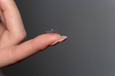 Bir kadının işaret parmağındaki kontakt lensin yakın çekimi. Modern görüş düzeltme teknolojileri ve günlük hayatta lenslerin kolaylığı. Göz bakımı ve göz doktoruna düzenli ziyaretler..