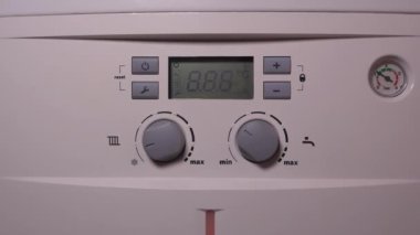 Bir kadının ellerinin yakın plan çekimi, kombine gaz kazanının güç düğmesine basıyor. Manikürlü el kazanı açmak için düğmeye basar ve kontrol paneli ışığa cevap olarak yanar..