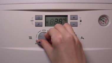 Bir kadının elinin yakın çekimi, ısıtma kontrol düğmesini ayarlamak virgül gaz kazanının. Manikürlü el ısıtma sistemini çalıştırmak için kadranı çeviriyor ve eve sıcaklık getiriyor..