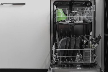 Bulaşık makinesinin içinde dikkatlice düzenlenmiş koyu tabaklar ve yeşil bardaklar zarif bir renk eşleşmesi yaratır. Temizlik ve organizasyon modern teknolojinin kolaylığını vurguluyor..