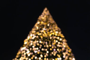 Noel ağacının bulanık silueti geceye karşı zar zor görülebiliyor, sadece parlak bokeh noktalarının çarpıcı ana hatlarını oluşturan çelenklerin yumuşak parıltısıyla..