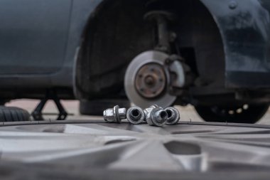 Bir araba tekerleğini değiştirme süreci. Sürgüler ve silinmiş bir tekerlek ön planda yatarken, arka planda bir krikonun üzerinde kaldırılmış bir araba görülebilir..