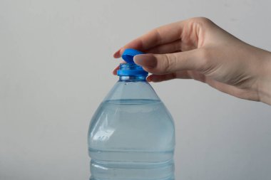 Bir su şişesini açmak: Şeffaf plastik bir su şişesinin mavi kapağını nazikçe büken bir elin yakın çekimi. İçindeki suyun ferahlatıcı berraklığı, susuz kalmamanın önemini vurgular..