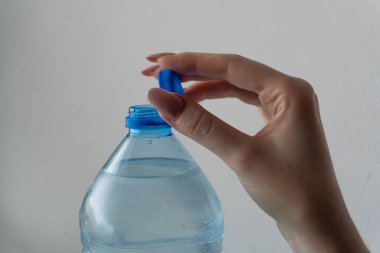 Bir kadının eli plastik bir şişeyi zarif bir şekilde açık bir kapakla tutuyor, bu da susuzluğu korumanın önemini ve ulaşılabilirliğini simgeliyor. Şişenin şeffaf tasarımı ve ergonomik şekli günlük kullanım için kolaylık sağlar.