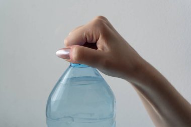 Bir kadın nazikçe tutarak plastik şişenin kapağını açar ve serin, temiz suyun tadını çıkarmaya hazırlanır. Elleri titizlikle hareket ediyor. Hareket halindeyken susuz kalmamanın basitliğini vurguluyor..
