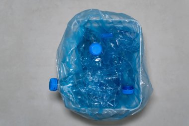 Plastik atık: Buruşmuş plastik su şişeleri ve mavi kapaklı bir çöp kutusu. Görüntü, atık ayrılmasının önemini vurguluyor.