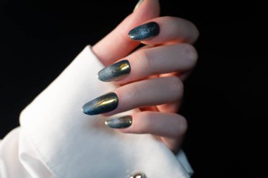 Contemporary manicure with a magnetic effect of cat-eye polish on a black background, shimmering with golden brilliance, pairs perfectly with evening outfits. This metallic manicure accentuates individuality and creativity. clipart