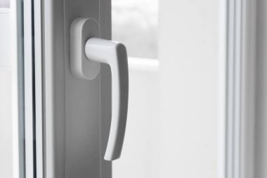 Modern Basitlik ve Fonksiyonellik: Kapalı çift camlı pencerenin beyaz plastik sapı parlak iç kısma karşıdır. Pencerenin temiz çizgileri ve minimalist tasarım modernliği ve pratiği vurguluyor.