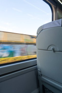 Dinamik ve sükunet: Dışında grafiti olan bir çitin bulanık dış hatlarını gösteren pencereli bir tren koltuğu arkası manzarası. Fotoğraf, dış dünyanın hareketini ve trenin içindeki sakinliği yansıtıyor..