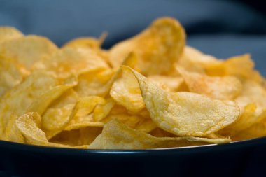 Tuzlu çerez yakın plan: mükemmel altın sarısı tonda, detaylarıyla yakalanmış tuzlu patates cipsi yığını. Mavi arkaplan ile karşıtlık bu çiplerin canlı renklerini vurguluyor, çekici bir görünüm yaratıyor.