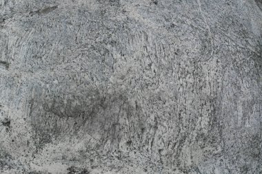 Taş dokusu: Karakteristik çatlaklar, mineral kaplamaları ve gri ve bejin doğal tonlarına sahip bir taşın kaba dokusuna yakın çekim. Taşın yüzeyi çok büyük görünüyor ve antik dağ kayalarına benziyor..