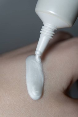 Makro 'da fosforlu kremin sivri uçlu bir borudan bir kadının elinin derisine nazikçe inen parlak fosforlu bir kremin yakın plan çekimi. Krem rengi hafif, kremalı ve ışıl ışıl..