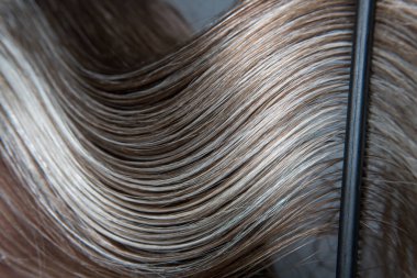 Doğal saç yapısı: Makro fotoğraf, parlak platin-gri ipliklerle dokunmuş düz kahverengi saçlar sergiliyor ve kontrastın ve doğal güzelliğin dokulu bir etkisini yaratıyor..