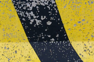 Uyarı sarı ve siyah boyalı aşınmış yol bariyeri: Bariyeri kaplayan siyah ve sarı çapraz şeritli desenli beton bir yüzeye yakın plan. Çatlamış boya ve açığa çıkmış beton yıpranmış bir etki yaratır..