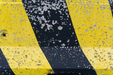 Yol bariyerinde sarı ve siyah boya uyarısı. Sarı bir tabanda siyah bir şerit, sayısız çizik ve çatlakla yol bariyerinin yüzeyini kaplar, güvenliği simgeler ve giysiyi simgeler.. 