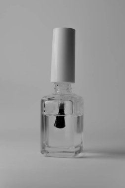 Beyaz arka planda açık bir tırnak cilası şişesi ve hafifçe vidalanmamış fırça: Çekim kozmetik ürünün minimalizmini ve çok yönlülüğünü vurguluyor.