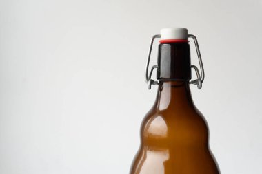 Kehribar cam şişenin parlak yüzeyi hafif ışığı yansıtırken, kapağı sıkıca kapatılmış, hem klasik çekiciliği hem de pratikliği vurguluyor..