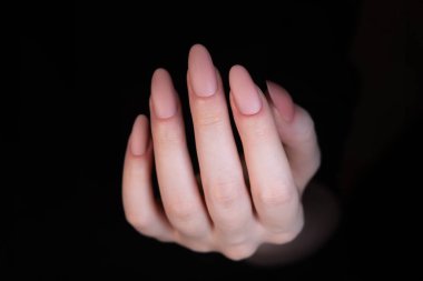 Oval şekilli uzatılmış tırnaklardaki bej renkli mat manikürü bitiş çizgisinin pürüzsüz dokusu manikürü şık ve minimalist yapar. Parmakları hafifçe kıvrılmış, çivilerin uzunluğunu ve şeklini gösteriyor..