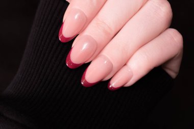 Feminen bir elde klasik kırmızı Fransız manikürü siyah bir arkaplanda zarif bir siluet, canlı çizgileri ve canlı rengi vurguluyor. Uçları parlak kırmızıya boyanırken, tırnak yatağı da nötr pembe bir ton olarak kalarak çarpıcı bir kontrast oluşturuyor..