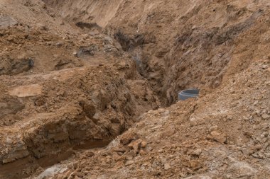 İnşaat alanında bir kazı alanı. Beton bir halka döşenmiş. Elektrik veya drenaj için tasarlanmış. Gevşek toprak yığınları ve açık katmanlı kayalar yapı sürecini aktaran dokulu, doğal bir zemin oluşturur..