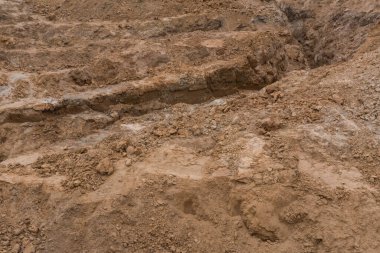 Görünür toprak ve kil tabakasıyla bir inşaat sahasında kazılmış arazi. Topraksı tonlar ve engebeli desenler, ağır makinelerin ve çevresel dönüşümün etkisini vurgular..
