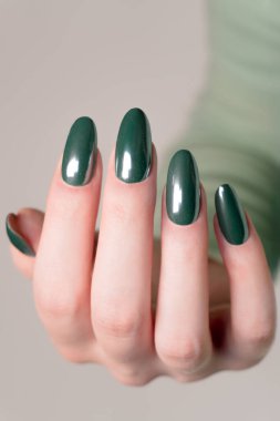 Düzgün şekilli oval tırnakları olan bir kadının eli. Lüks, koyu yeşil bir renge boyanmış. Sofistike, özgüvenli ve ebedi tırnak sanatı tarzında..
