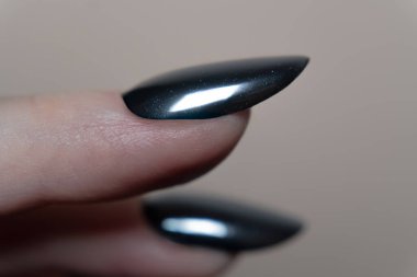 Işığı yüzeyden yansıtan parlak, siyah oval tırnakların detaylı bir çekimi. Bir klasiğin görkemli ve modern görüntüsü. Tırnaklardaki yansımalar boyut ve derinlik ekler, cilalı görünümü güçlendirir..
