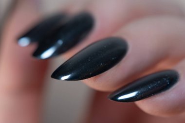 Aynaya benzer bir ışıltıyla siyah manikürün yakın çekimi, bitirmenin pürüzsüzlüğünü ve hassasiyetini vurguluyor zarafet ve eğilimin mükemmel bir karışımı.