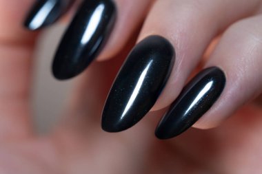 Tırnakların oval şeklini vurgulayan bir makro çekim, koyu siyah parlak cilalı çarpıcı bir görünüş için sofistike ve şık bir seçim..