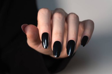 İyi bakımlı bir elde güzelce cilalanmış siyah tırnaklar, tarafsız bir arkaplanda fotoğraflanmış her ayrıntıda stil, temizlik ve güzelliğin bir örneği..