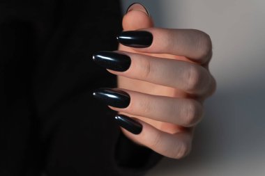 Uzun oval tırnaklarda parlak siyah manikür zarif ve cesur bir görünüm aynaya benzer bir parlaklıkla sofistike ve kendine güveni ön plana çıkaran.