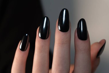 Siyah ve beyaz arka planda dinlenen bir elde siyah manikür karşıtlıkların oyunu resme sanatsal dışavurumluluk katar. Çiviler yuvarlak, badem benzeri bir şekilde düzgünce şekillenmiş..