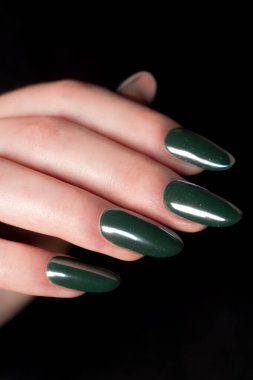 Koyu bir arka planda dinlenen parlak, koyu yeşil tırnaklar lüks bir his ve cesur bir kişiliğe sahip modaya uygun, karamsar bir bakış..