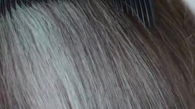 Bir tarağın dişlerinden süzülen parlak gri saçlar, hareket halindeki gümüş ipliklerin dokusunu ve yumuşaklığını yakalar..