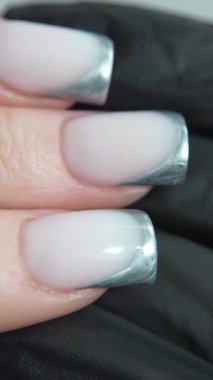 Parlak gümüş kenarlı Fransız manikürü çizgi hassasiyeti ve mükemmel simetriye odaklanır. Fransız manikürü eli giyilebilir bir sanat parçasına dönüştürür. Teknisyenin siyah eldiveni karşıtlığı ve profesyonelliği vurguluyor.